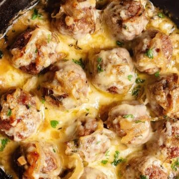 Cheesy meatballs in a creamy sauce, topped with herbs and served in a black cast iron skillet—perfect for those seeking delicious high-protein recipes.