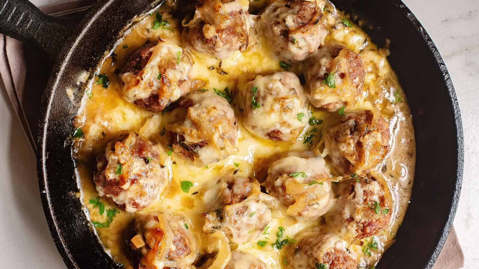 Cheesy meatballs in a creamy sauce, topped with herbs and served in a black cast iron skillet—perfect for those seeking delicious high-protein recipes.