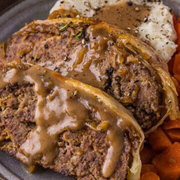 Two slices of meatloaf with gravy, mashed potatoes, and cooked carrots on a plate—a comforting meal inspired by classic vintage recipes.