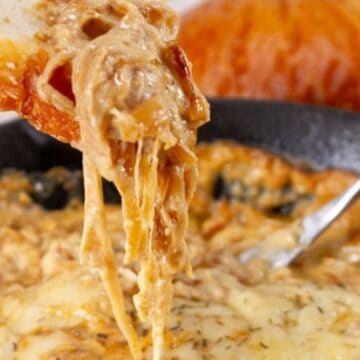 A slice of bread dipped into a hot, cheesy onion dip in a skillet, with cheese stretching between them—one of those irresistible budget comfort recipes perfect for sharing.