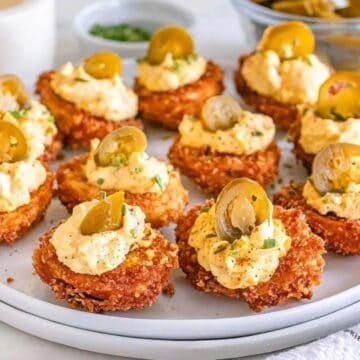 A plate of crispy fried bites topped with creamy filling and sliced jalapeños, arranged on a white plate.