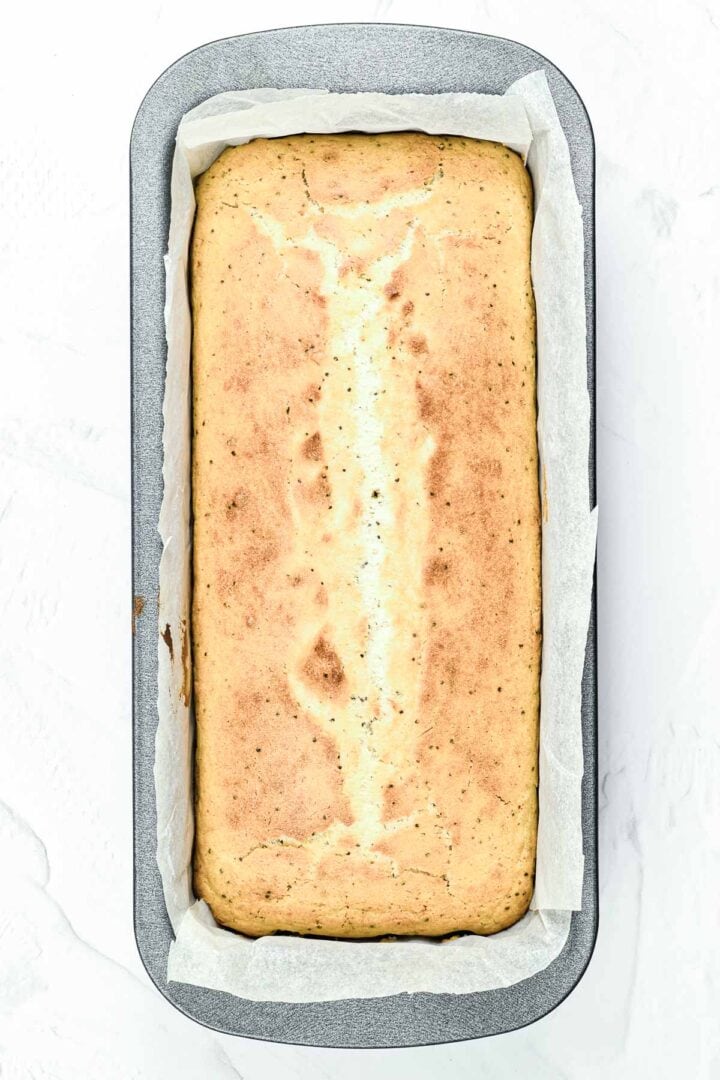 A baked loaf of bread in a parchment-lined loaf pan, viewed from above on a white surface.