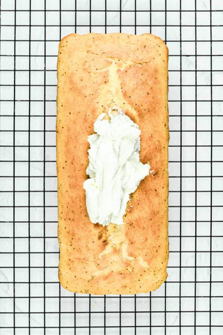 Loaf cake on a cooling rack with a dollop of white frosting spread down the center.