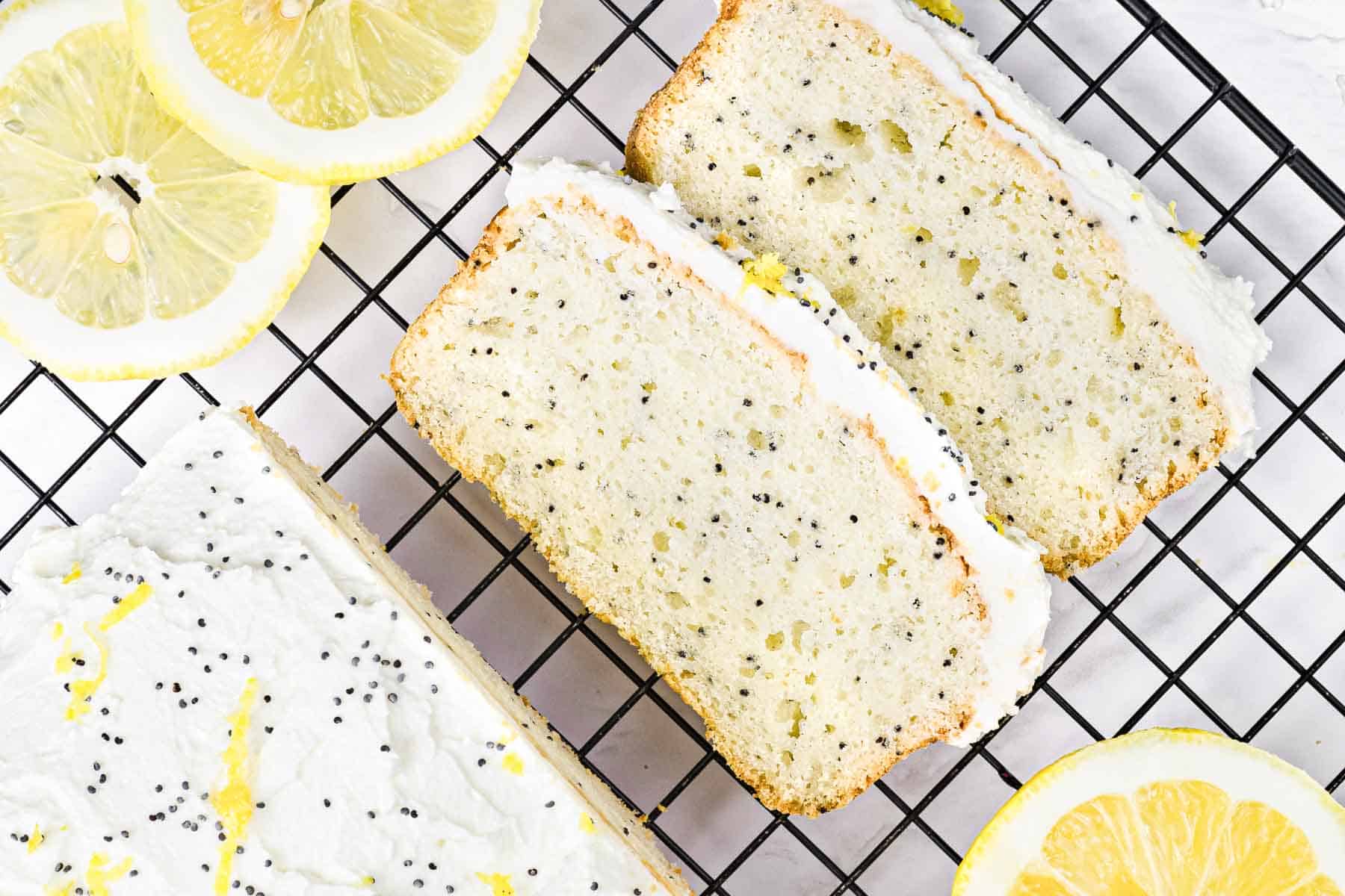 Sliced lemon poppy seed loaf with white icing on a cooling rack, surrounded by lemon slices.