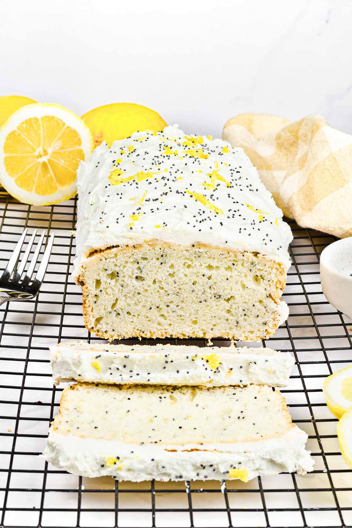 Lemon poppy seed loaf with white icing and lemon zest on a cooling rack, next to sliced lemons.
