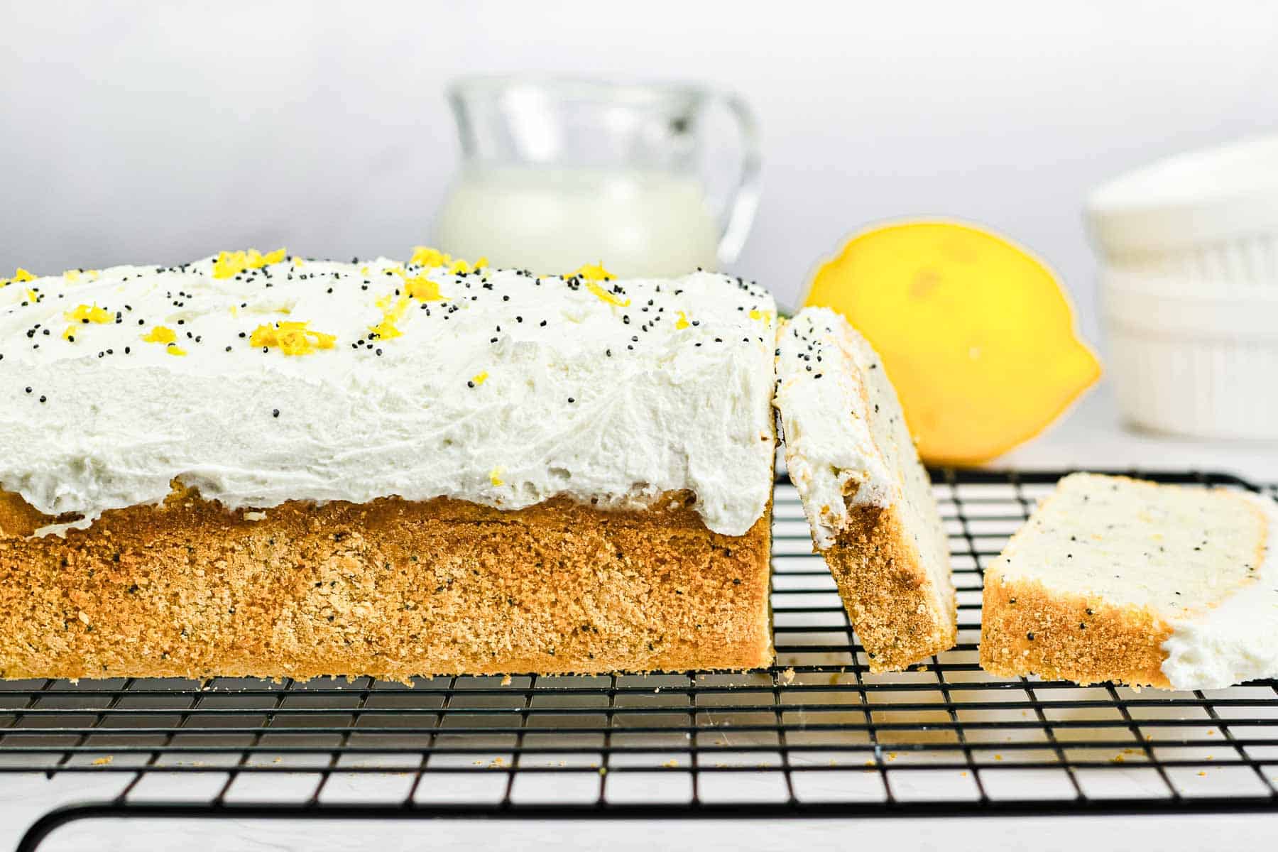Lemon poppy seed loaf with white frosting on a cooling rack, garnished with lemon zest and poppy seeds.
