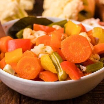 A bowl of mixed pickled vegetables, including carrots, celery, and peppers, with a wooden spoon.