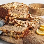 Gluten-Free Lemon Almond Loaf sliced on a wooden board, topped with sliced almonds, served with fresh lemon wedges on the side.
