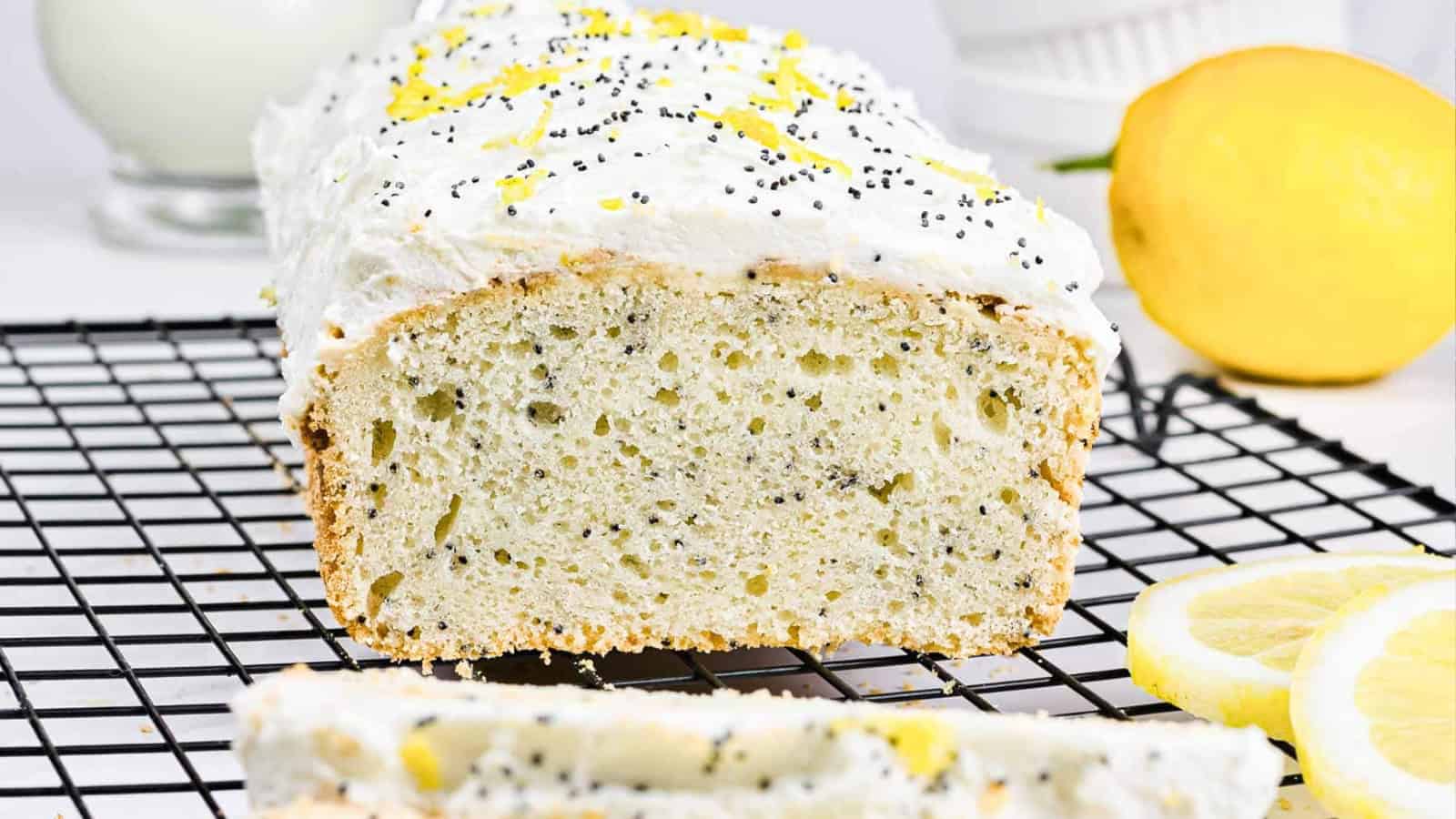 A sliced lemon poppy seed loaf with white icing, lemon zest, and poppy seeds on a cooling rack.