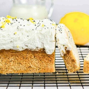 Lemon poppy seed loaf with white frosting, lemon zest, and a sliced lemon on a cooling rack.