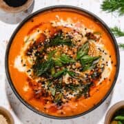 A bowl of creamy tomato soup topped with fresh herbs, sesame seeds, and a drizzle of oil—perfect alongside a spicy Gochujang Tahini Cabbage Soup.