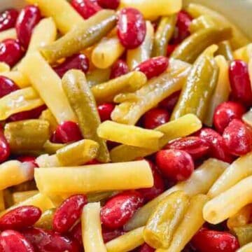 A close-up of a three bean salad with kidney beans, yellow wax beans, and green beans in a bowl.