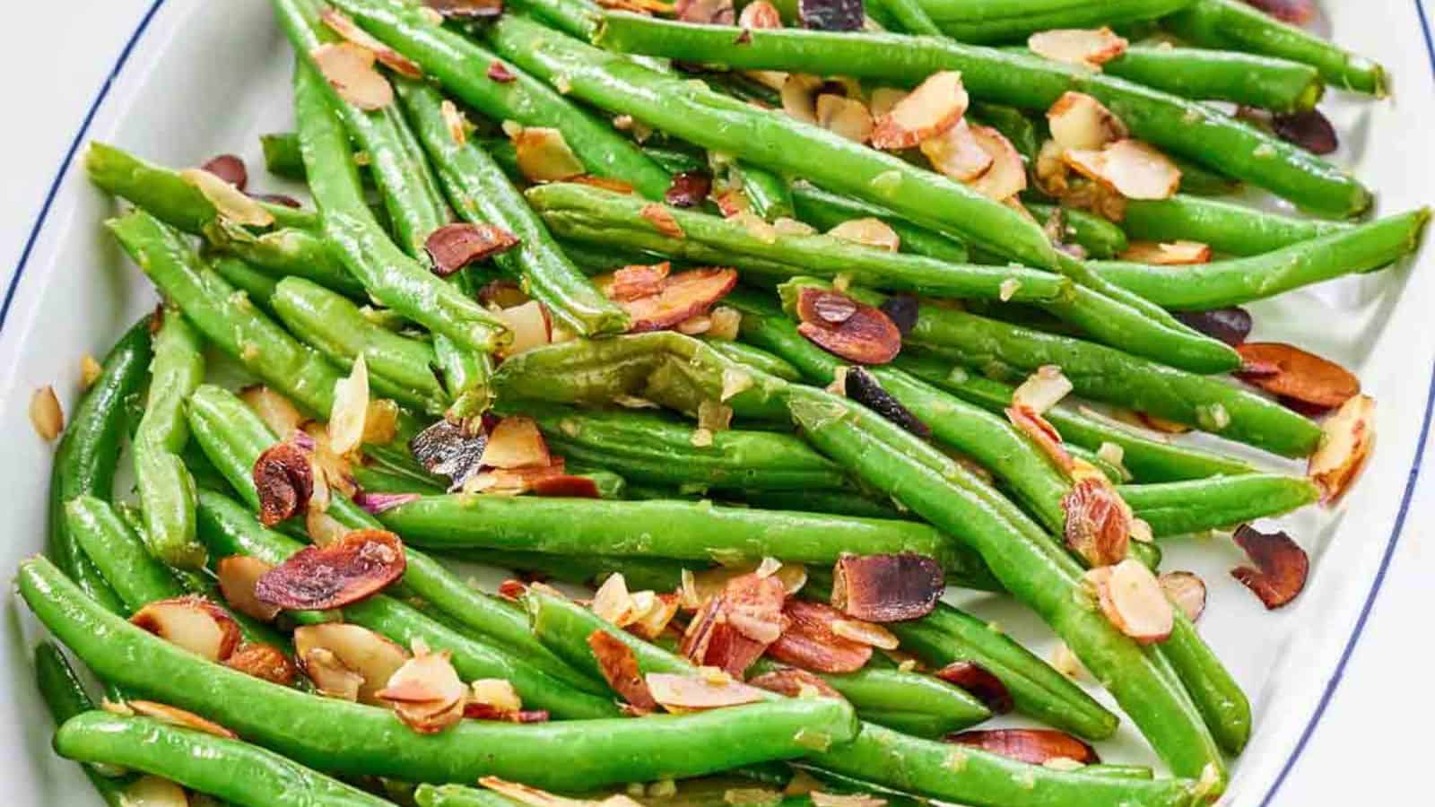 Green beans saut&eacute;ed with sliced toasted almonds on a white plate with a blue rim.