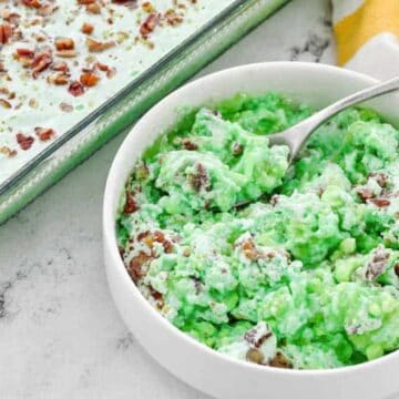 A bowl of green Watergate salad with chopped pecans, next to a dish of the same and a yellow-striped towel.