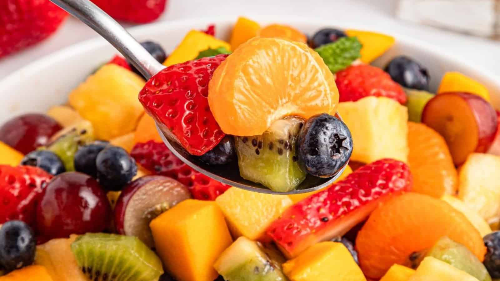 A spoonful of mixed fresh fruit including strawberry, mandarin, blueberry, kiwi, and more above a fruit salad bowl—perfect for your favorite brunch recipes.