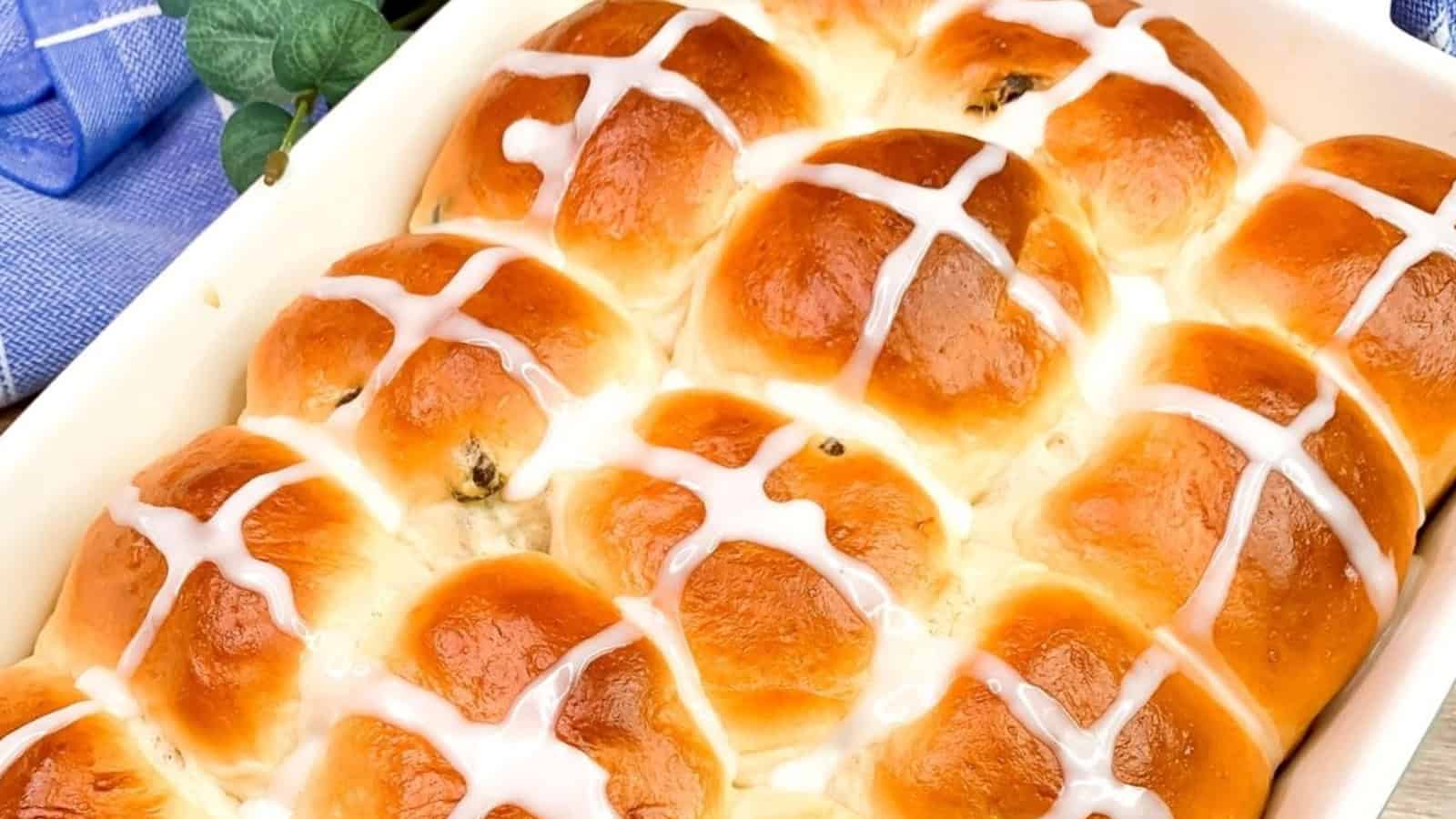 Golden brown hot cross buns in a baking dish, topped with white icing crosses.