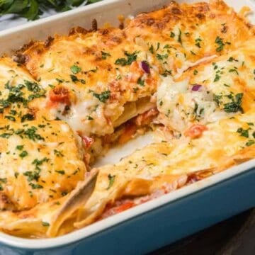 A cheesy baked lasagna in a blue dish, with a square piece removed and herbs sprinkled on top.