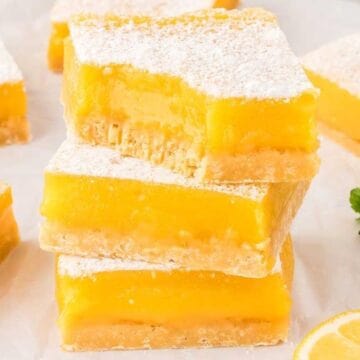 Three stacked lemon bars dusted with powdered sugar, with lemon slices and mint leaves nearby—a classic treat that brings retro desserts to life.