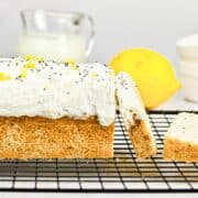 Lemon poppy seed loaf with white frosting and lemon zest, on a cooling rack with a lemon and milk in background.