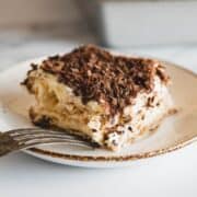 A slice of tiramisu topped with chocolate shavings on a plate with a fork.
