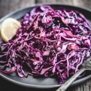 Mayo Purple Cabbage Slaw with shredded red cabbage, served on a dark plate with a lemon wedge and fork.