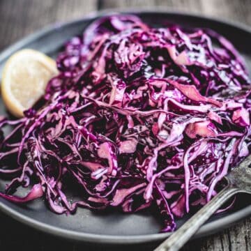 Mayo Purple Cabbage Slaw with shredded red cabbage, served on a dark plate with a lemon wedge and fork.