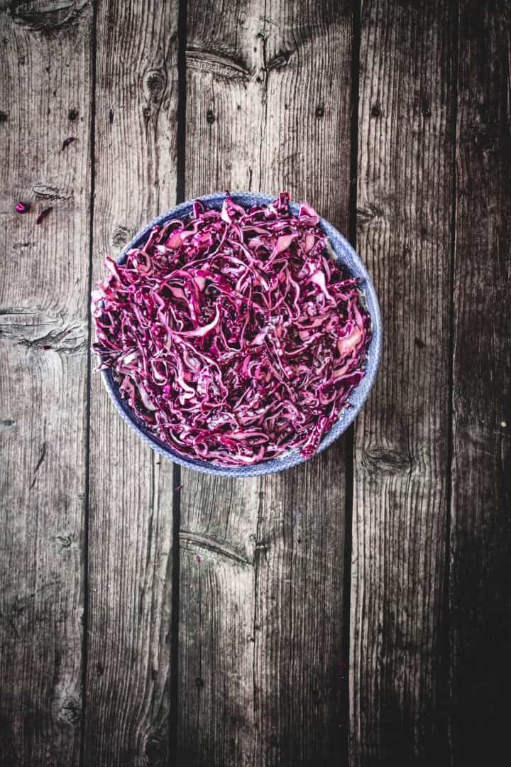 A blue bowl filled with shredded red cabbage, perfect for a Mayo Purple Cabbage Slaw, sits on a rustic wooden surface.