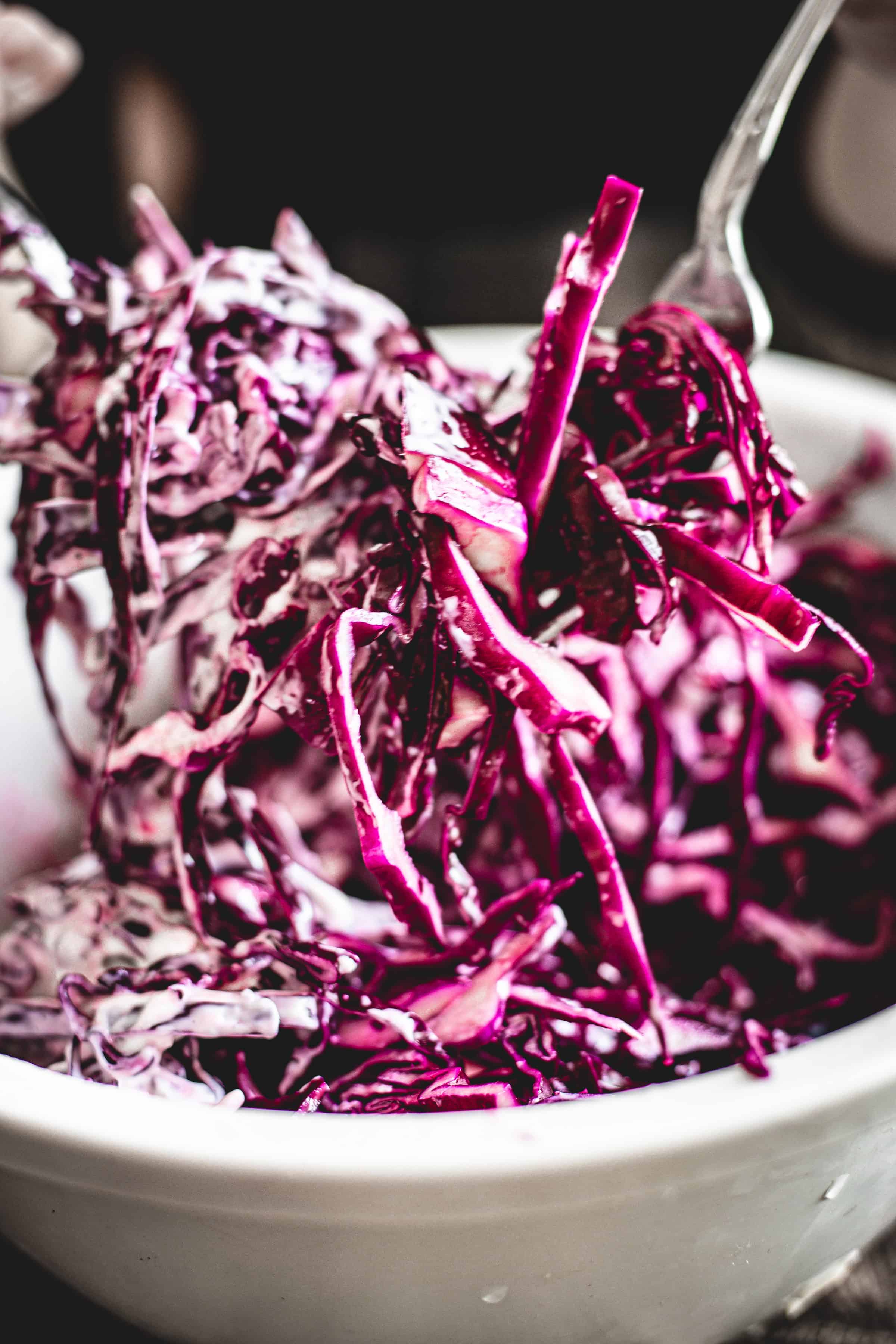 Mayo Purple Cabbage Slaw mixed with creamy dressing in a white bowl, served with metal tongs.