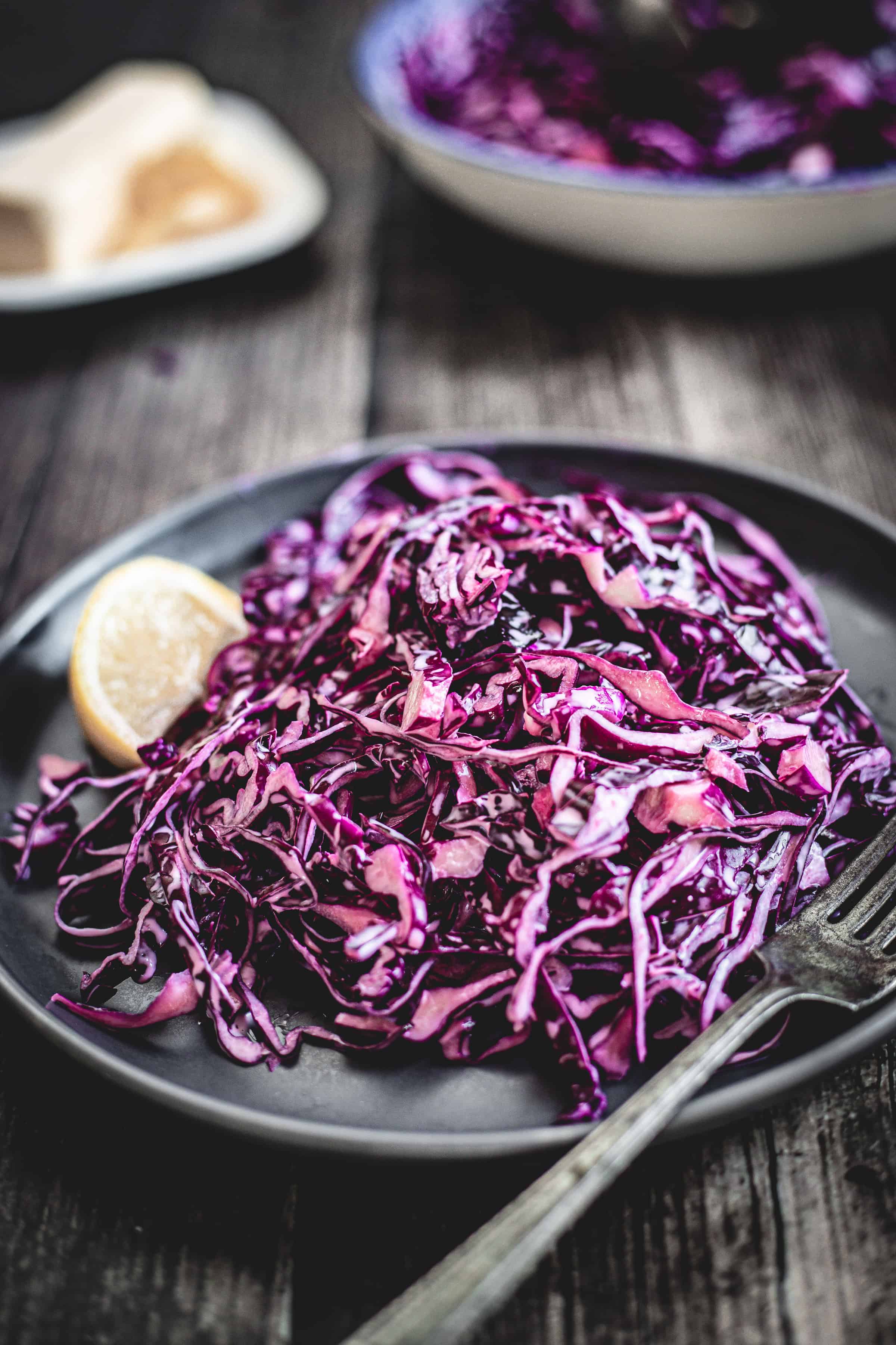 Mayo Purple Cabbage Slaw served with a lemon wedge on a dark plate, fork beside, atop a rustic wooden table.