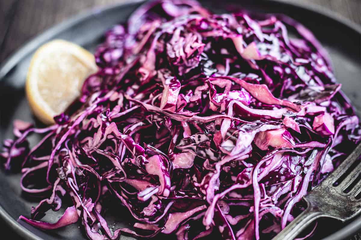 Mayo Purple Cabbage Slaw served on a dark plate with a lemon wedge and a fork.