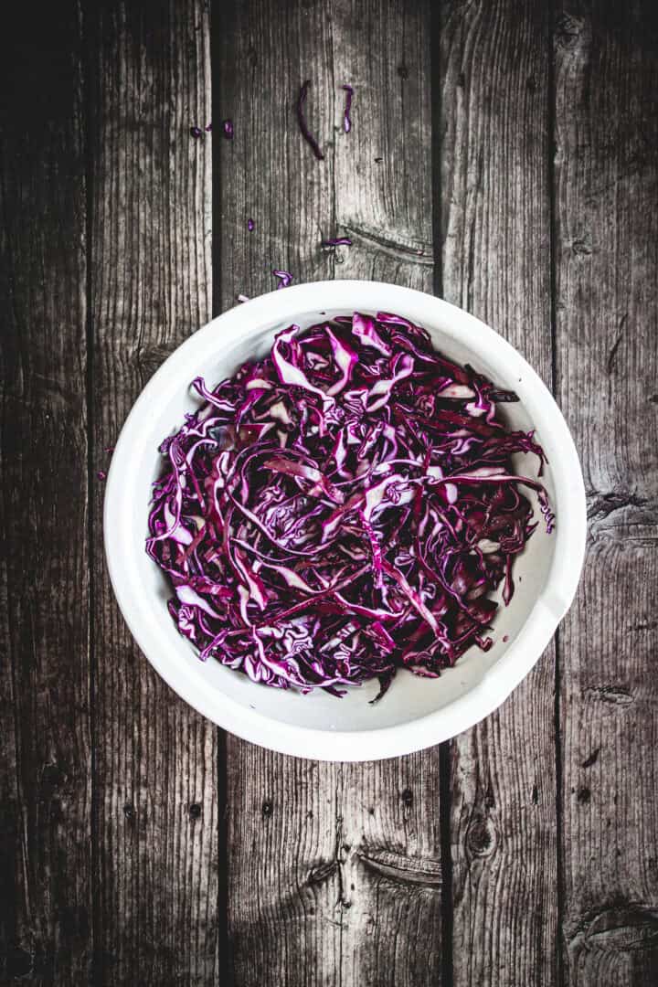 Mayo Purple Cabbage Slaw in a white bowl on a rustic wooden surface.