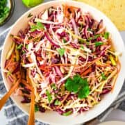 A bowl of colorful Mexican Coleslaw with shredded cabbage, carrots, and fresh cilantro, served with wooden utensils.