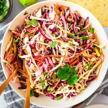 A bowl of colorful Mexican Coleslaw with shredded cabbage, carrots, and fresh cilantro, served with wooden utensils.