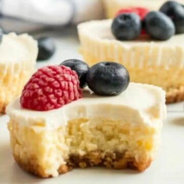 Mini cheesecakes topped with blueberries and raspberries—one with a bite taken out—make a delightful addition to your tea party recipes.