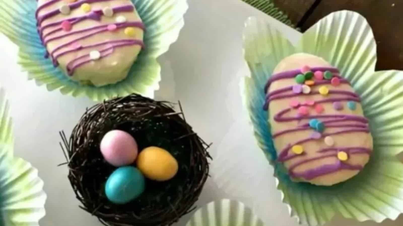 Mini egg-shaped cakes with purple frosting and colorful sprinkles.