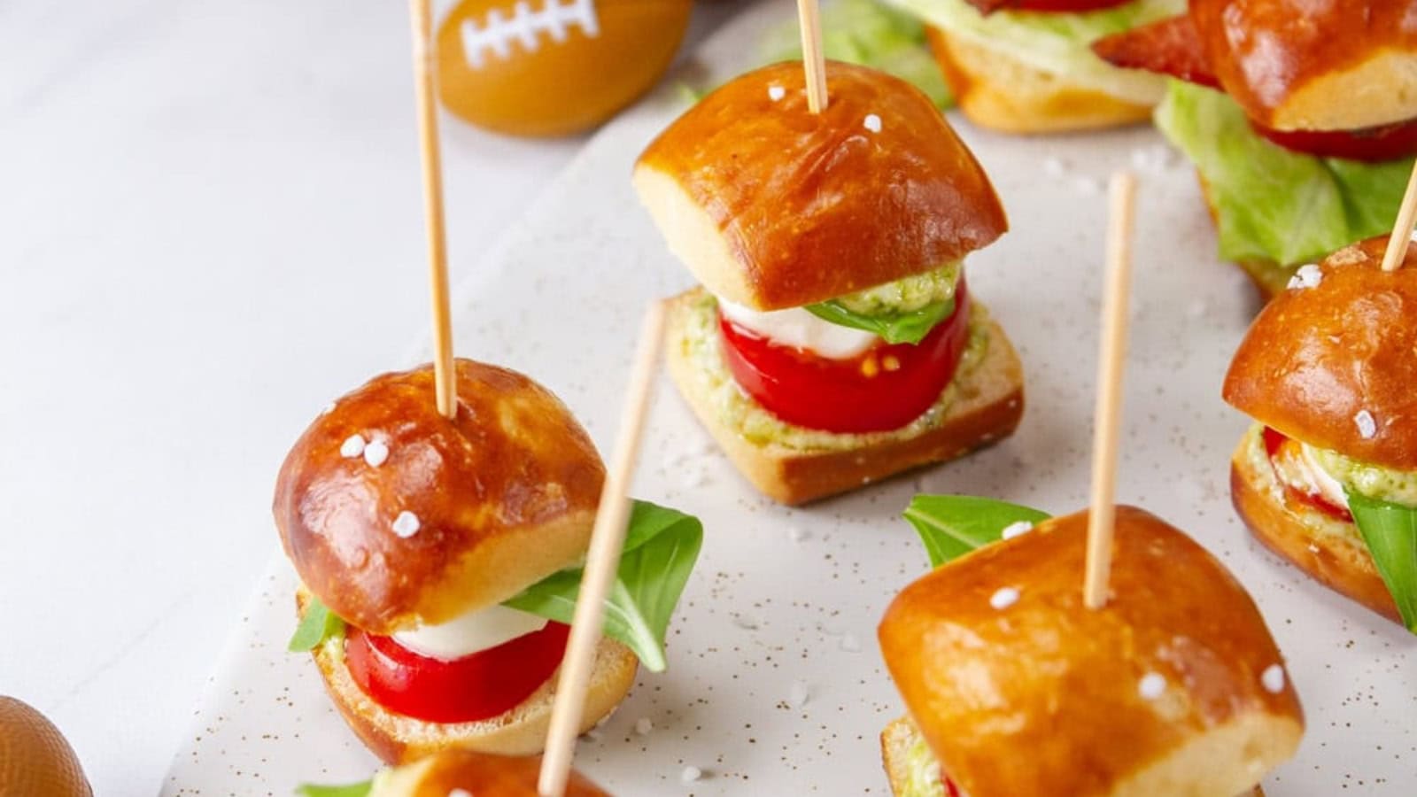 Appetizers featuring mini sandwiches with tomato, mozzarella, basil, and pesto on pretzel buns, each secured with a toothpick.