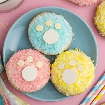 Colorful cookies with paw-print designs on a blue plate, surrounded by straws and a glass of milk.