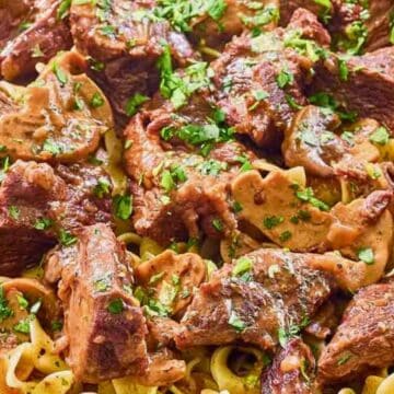 Beef stroganoff with mushrooms served over egg noodles, garnished with chopped parsley.