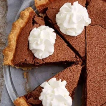 A chocolate pie with a flaky crust, sliced and topped with dollops of whipped cream.