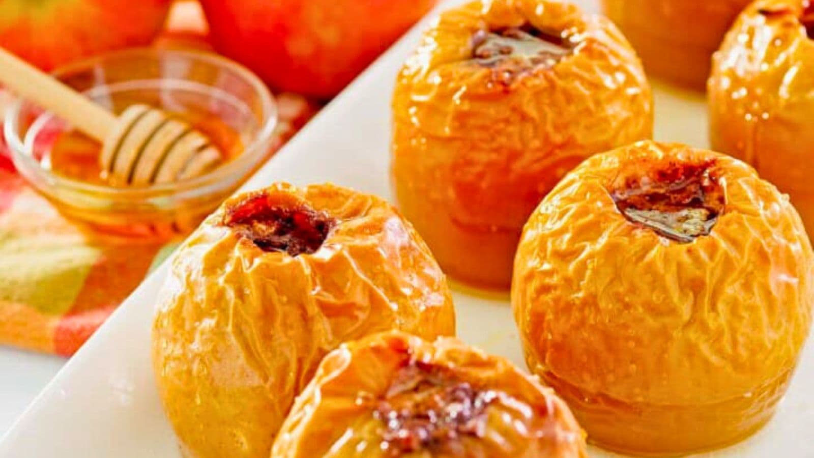 Baked apples with a sweet filling on a white plate, with a dish of honey and a honey dipper in the background.