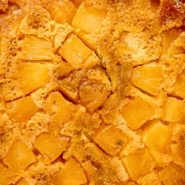 Golden pineapple upside-down cake on a white plate, with caramelized pineapple chunks on top.