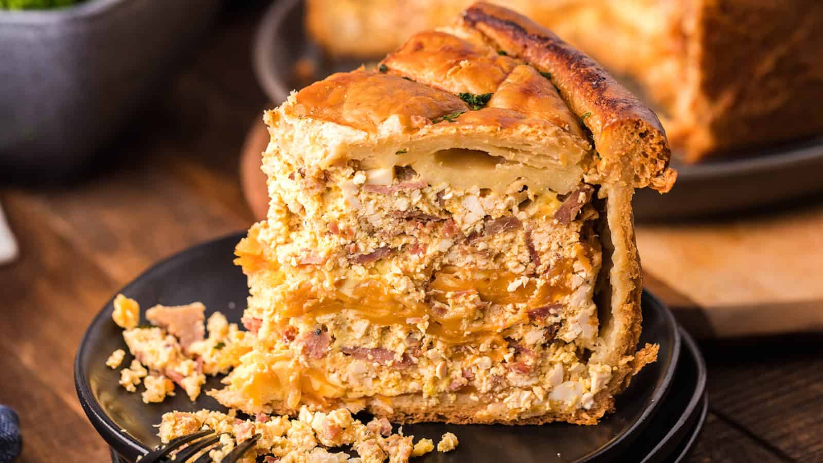 A thick slice of savory pie with layers of meat, eggs, and pastry sits on a black plate.