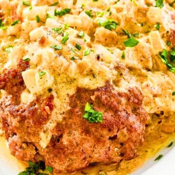 Meatloaf topped with creamy sauce and chopped herbs, served on a white plate.