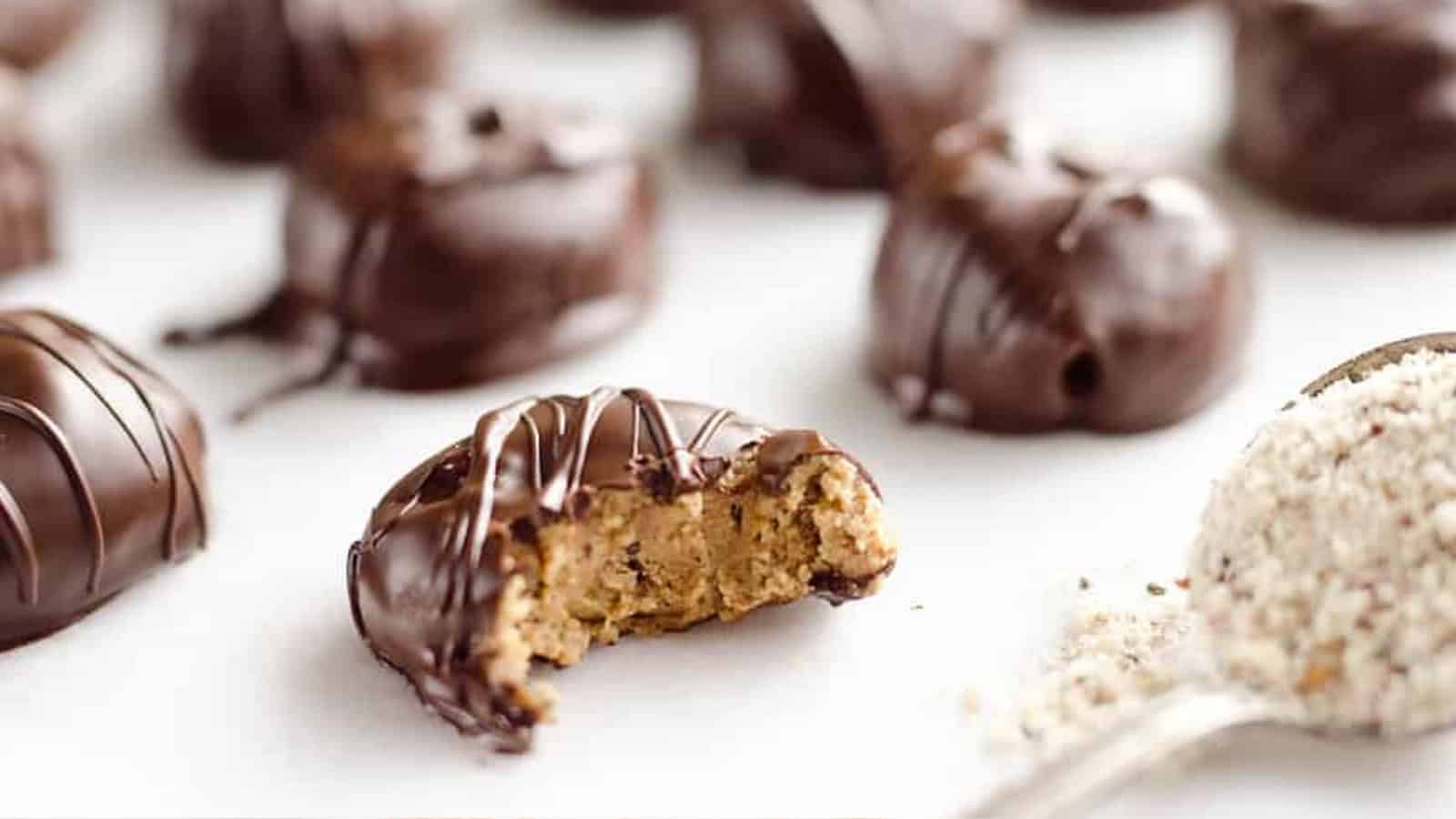 Chocolate-coated truffles with one bitten open, revealing a nutty vegetarian comfort foods filling, and a spoonful of ground nuts nearby.