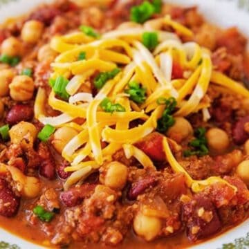 A plate of chili with beans, chickpeas, shredded cheese, and chopped green onions on top—perfect for easy pantry recipes.