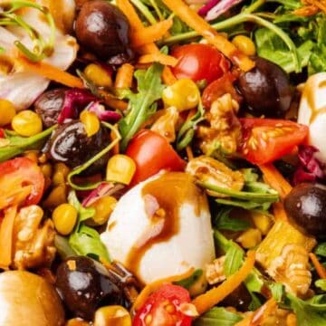Colorful salad with cherry tomatoes, mozzarella, olives, corn, arugula, carrots, walnuts, and balsamic dressing.