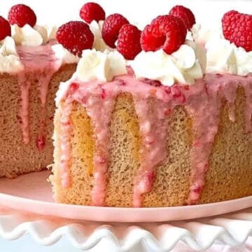 A delightful Easter cake featuring sponge layers with pink glaze, whipped cream, and fresh raspberries on top, with one slice cut out.