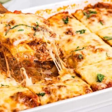 A slice of cheesy baked lasagna being lifted from a pan, with melted cheese stretching.