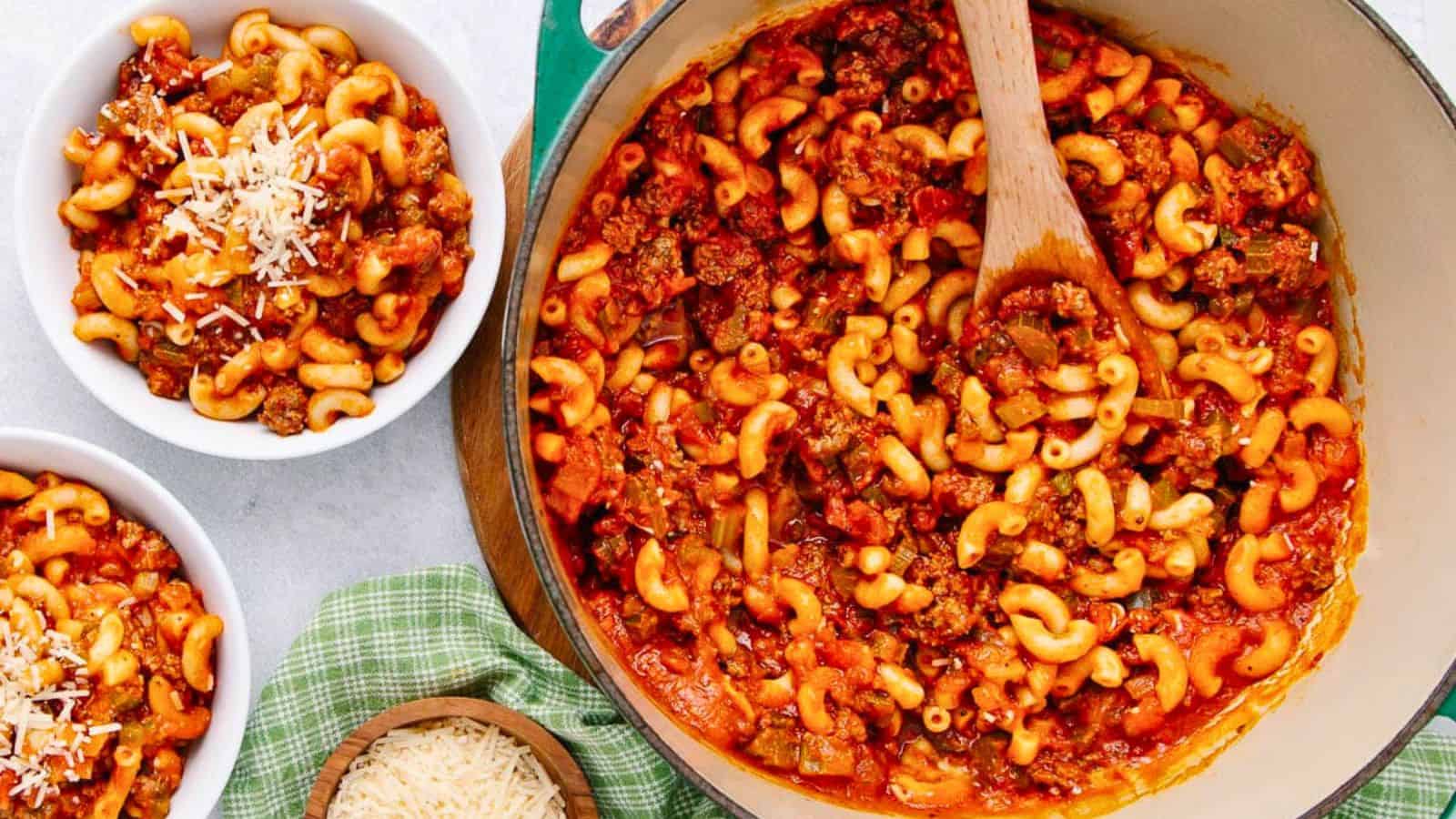 A pot of macaroni with meat sauce and bowls of pasta topped with grated cheese on the side.