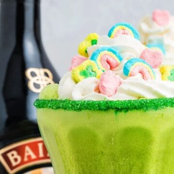 Green milkshake with whipped cream and colorful marshmallows, beside a bottle of Baileys Irish Cream.